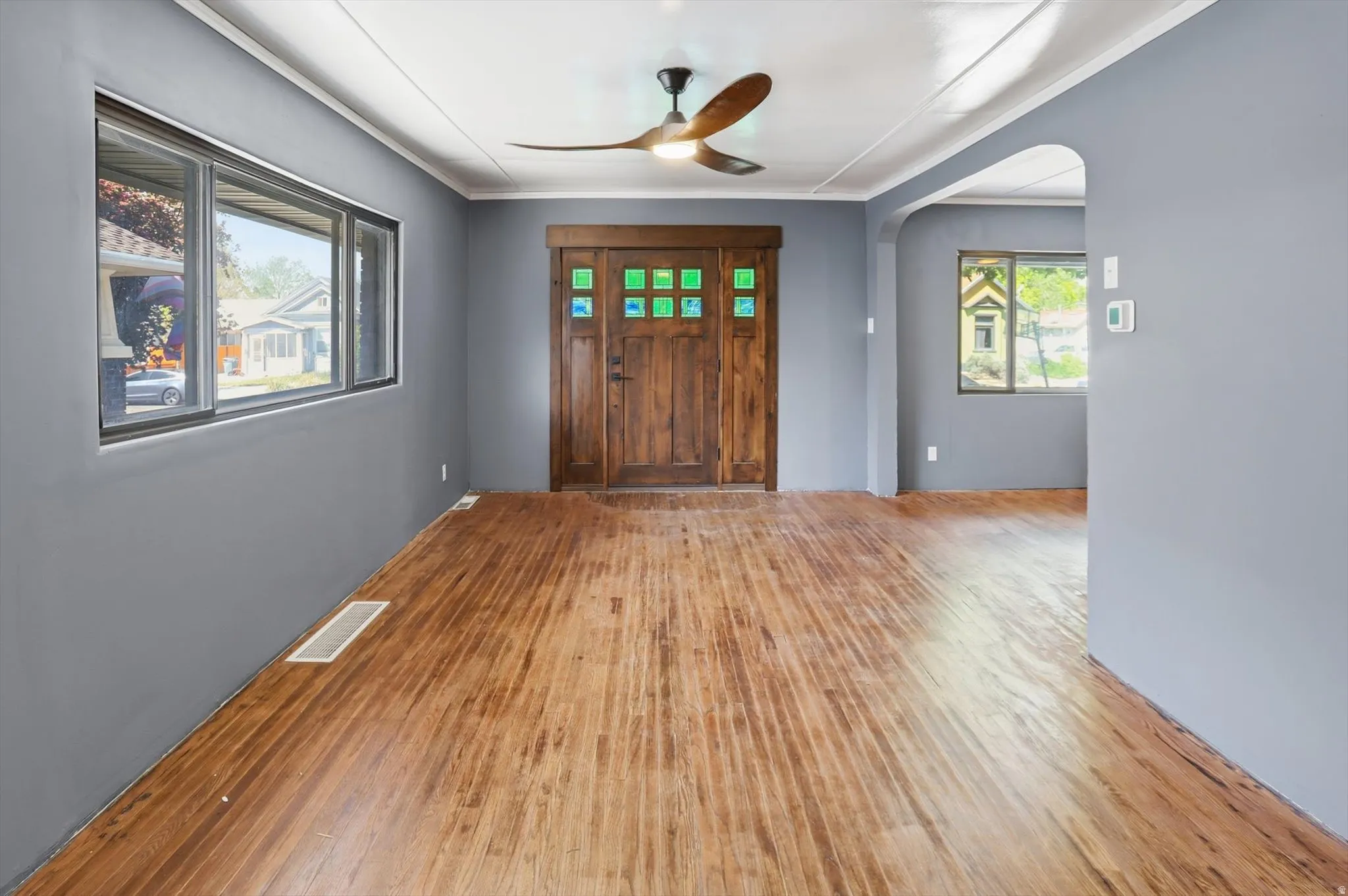 Foyer featuring arched walkways, light wood-style flooring, a ceiling fan, and ornamental molding