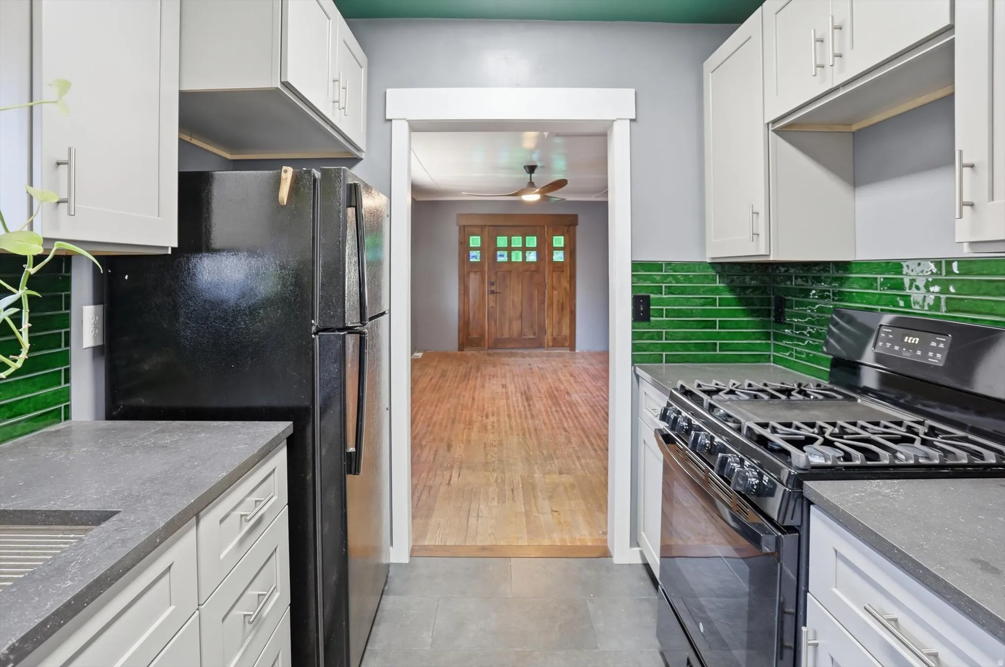 Kitchen with black appliances, white cabinetry, dark stone countertops, and ceiling fan