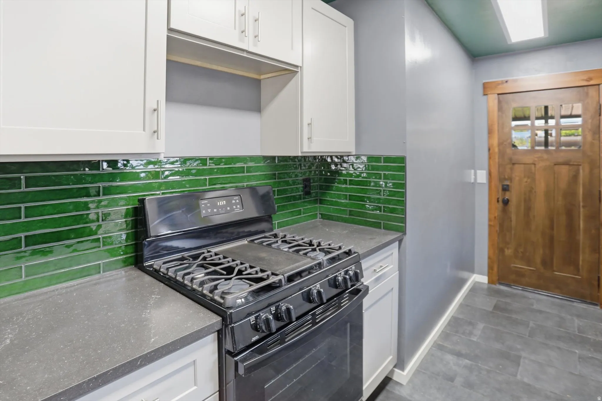 Kitchen with black gas range oven, white cabinets, dark stone countertops, and decorative backsplash
