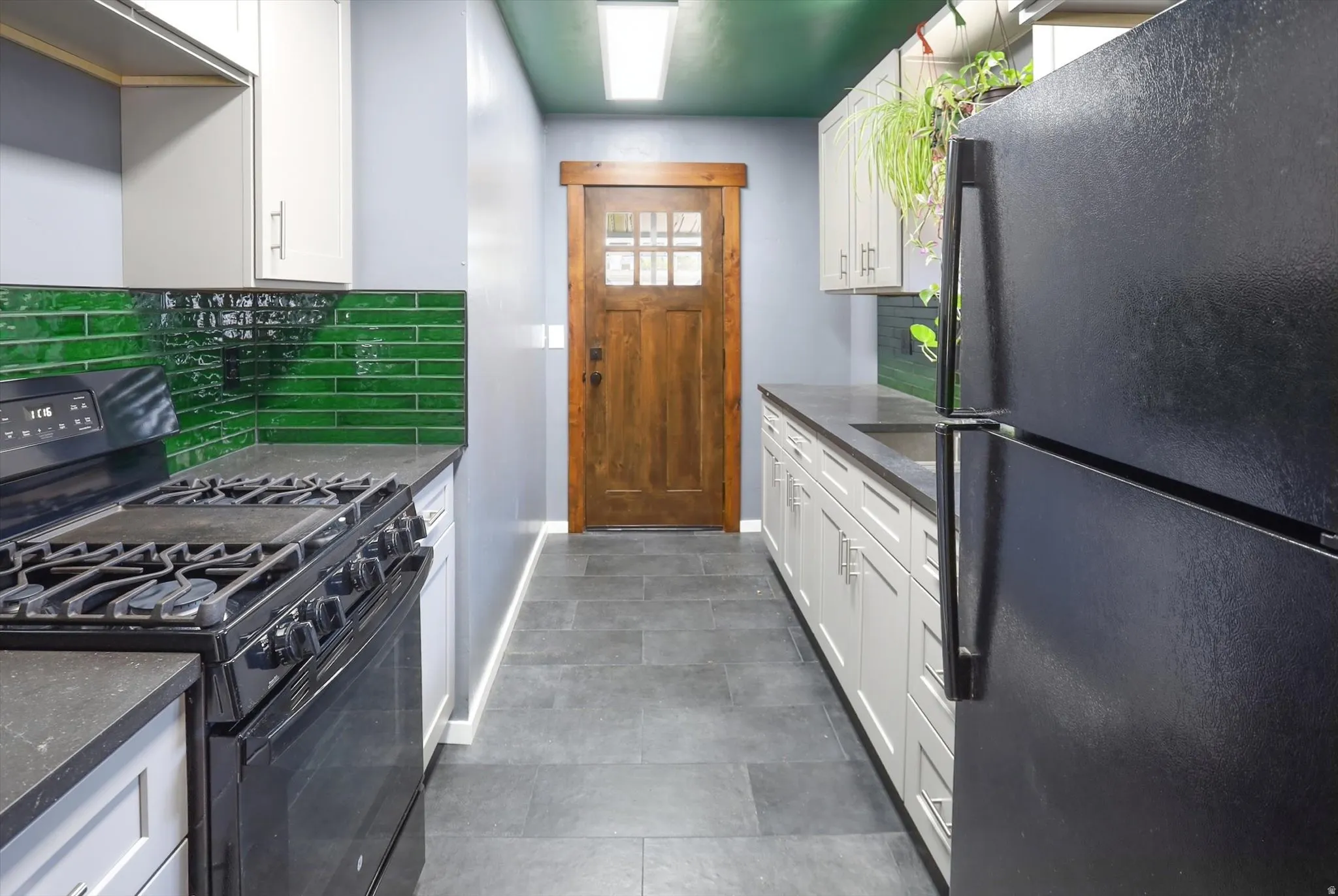 Kitchen with black appliances, white cabinets, dark stone countertops, and backsplash