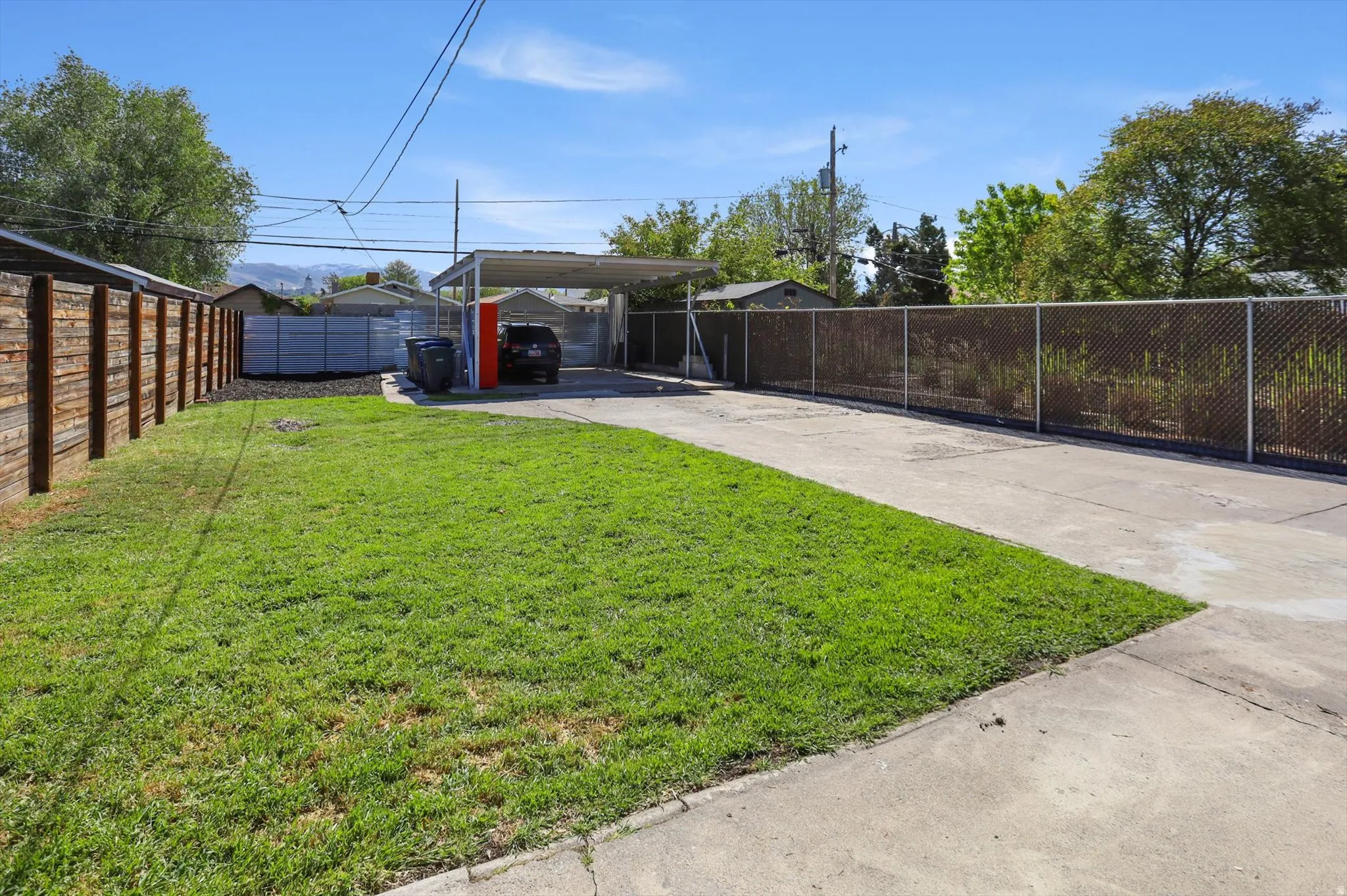 Fenced backyard featuring a detached carport, concrete driveway, and an outbuilding