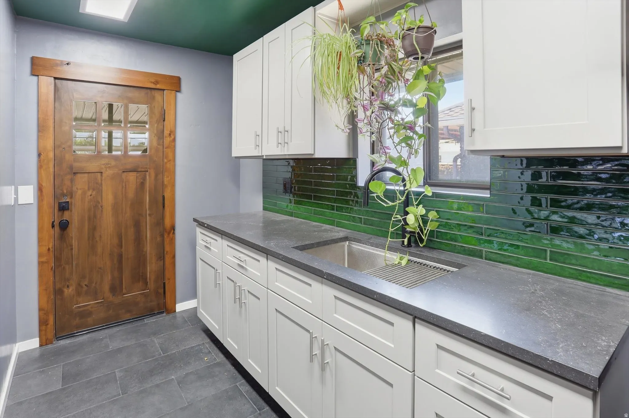 Kitchen featuring white cabinets, decorative backsplash, dark tile patterned floors, and dark stone countertops
