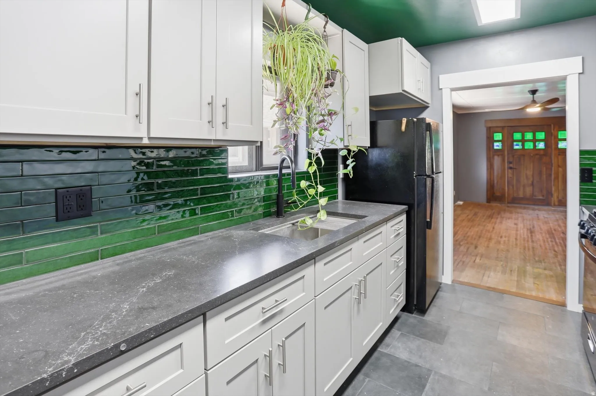 Kitchen with white cabinetry, freestanding refrigerator, tasteful backsplash, dark stone counters, and a ceiling fan