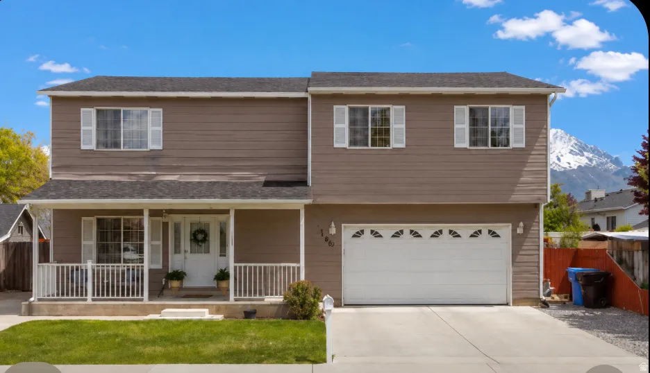 Two-story residence featuring a covered front porch with white railing, a two-car garage with decorative windows, and a paved driveway