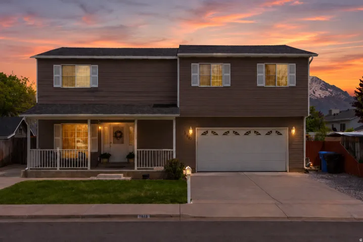 Two-story residence featuring a covered front porch with white railing, a two-car garage with decorative windows, and a paved driveway