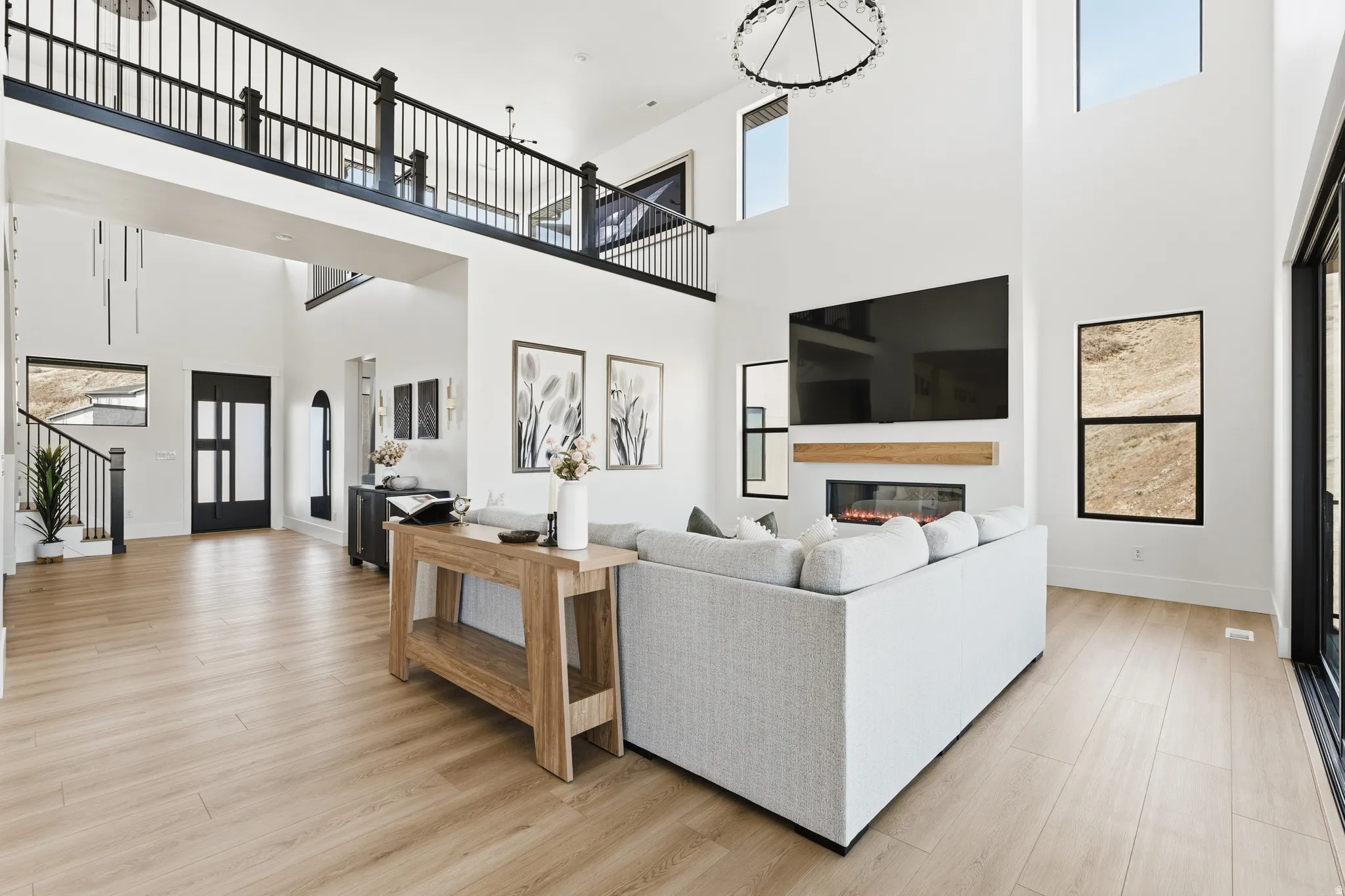 Living area with light wood-style floors, a glass covered fireplace, and a high ceiling