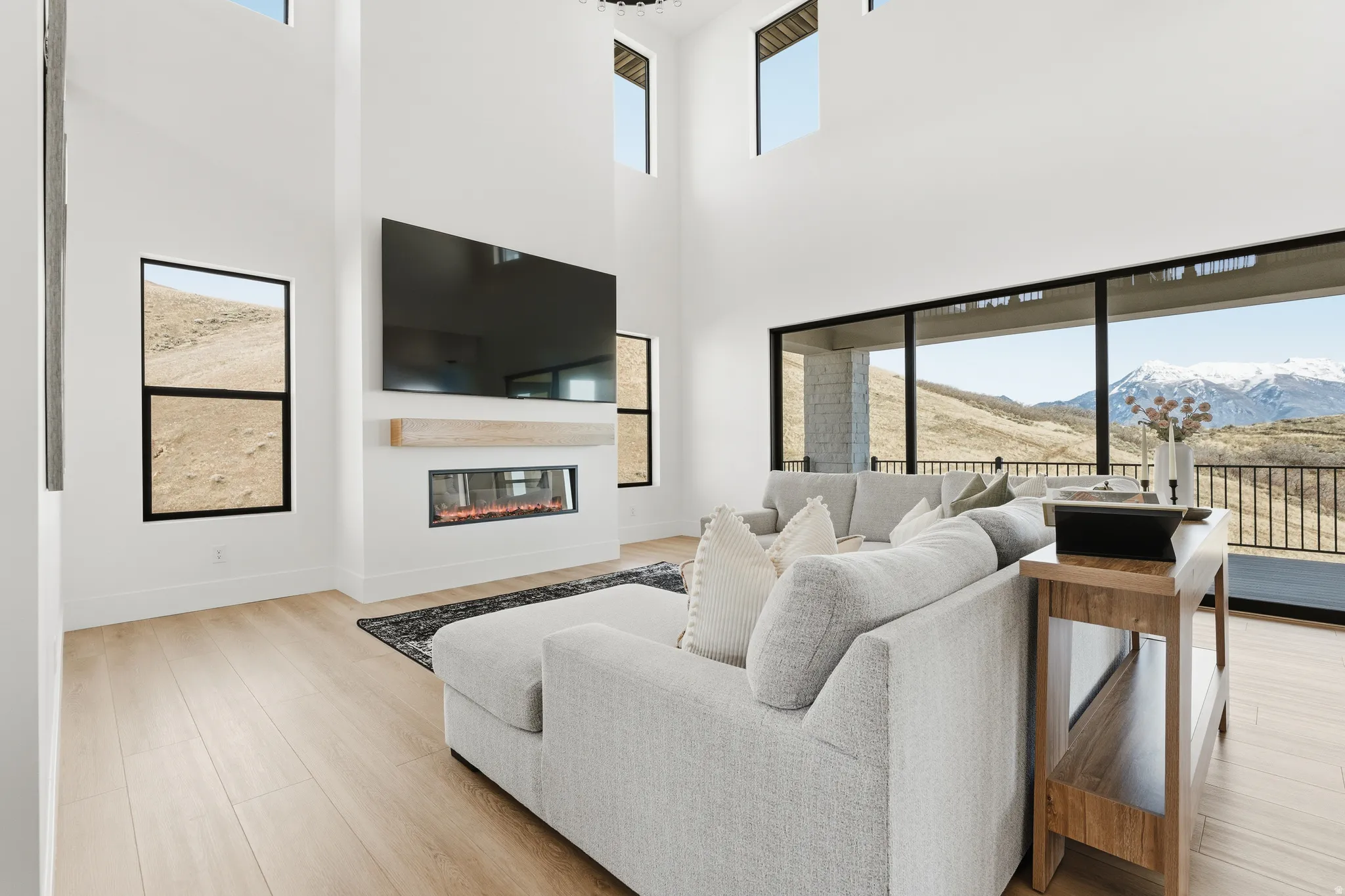 Living room with a glass covered fireplace, light wood-style floors, and a high ceiling