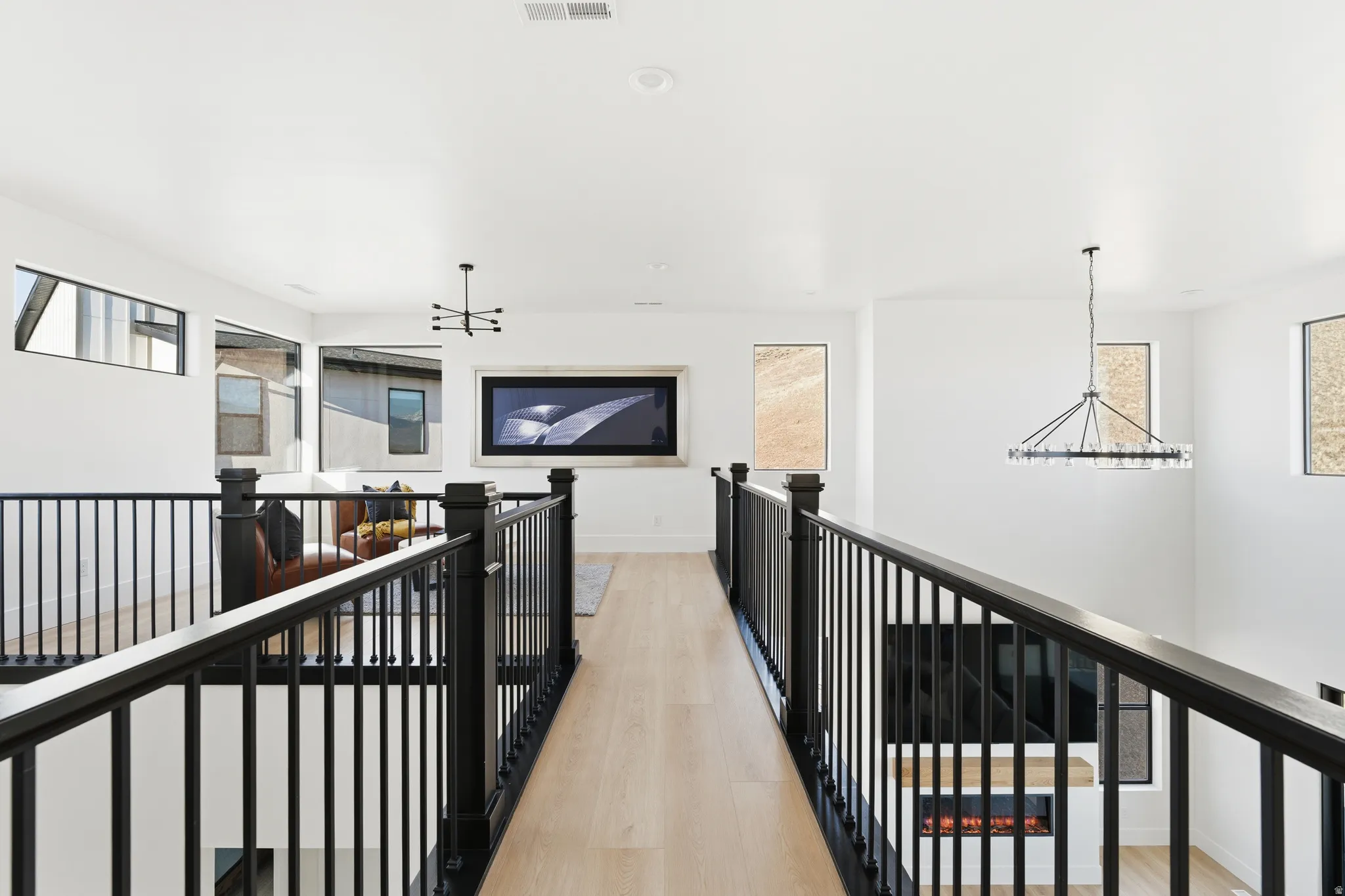 Hall featuring suspended lighting, light wood finished floors, and an upstairs landing