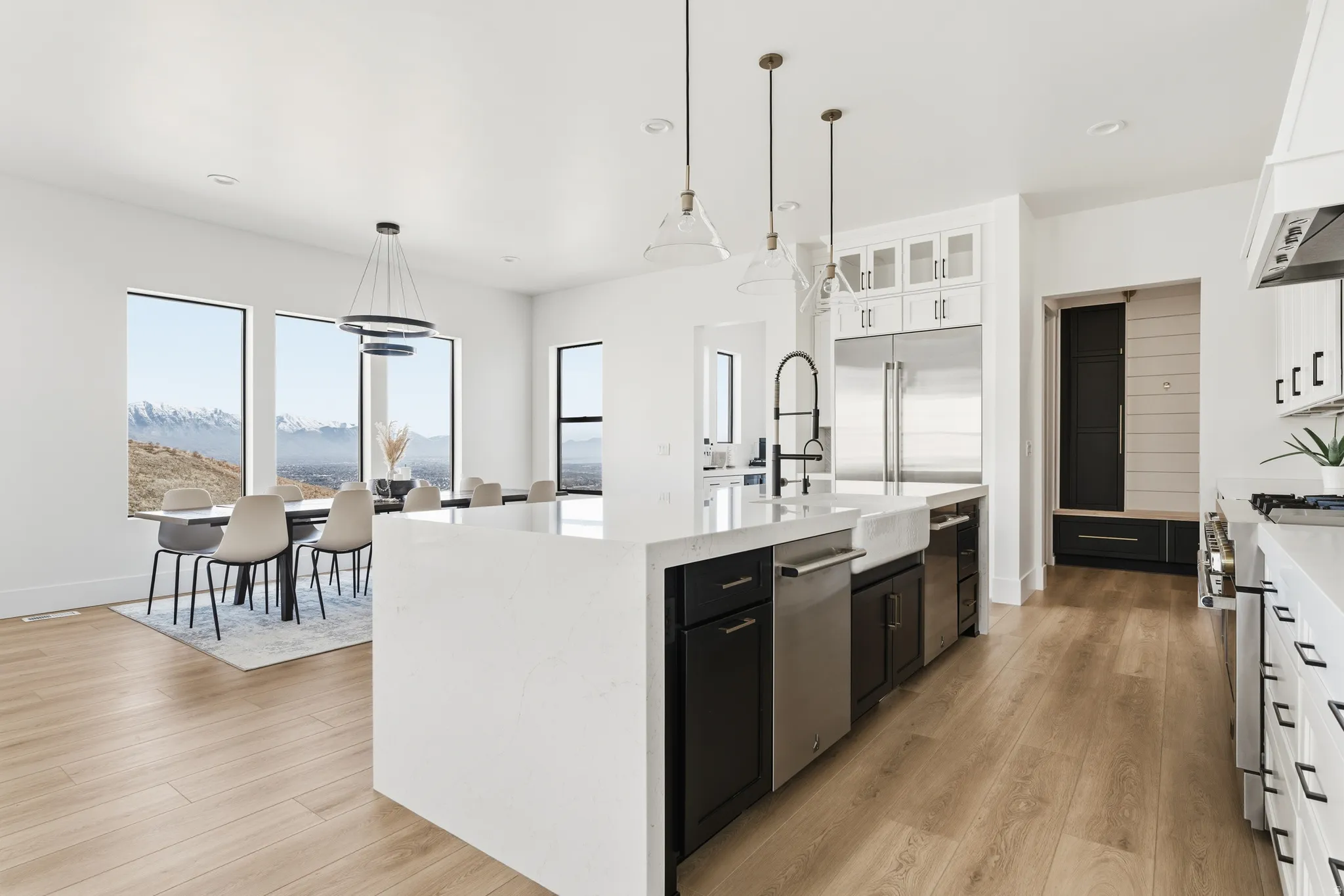 Two tone kitchen with dual tone cabinetry, light stone countertops, light wood finished floors, decorative light fixtures, and an island with sink