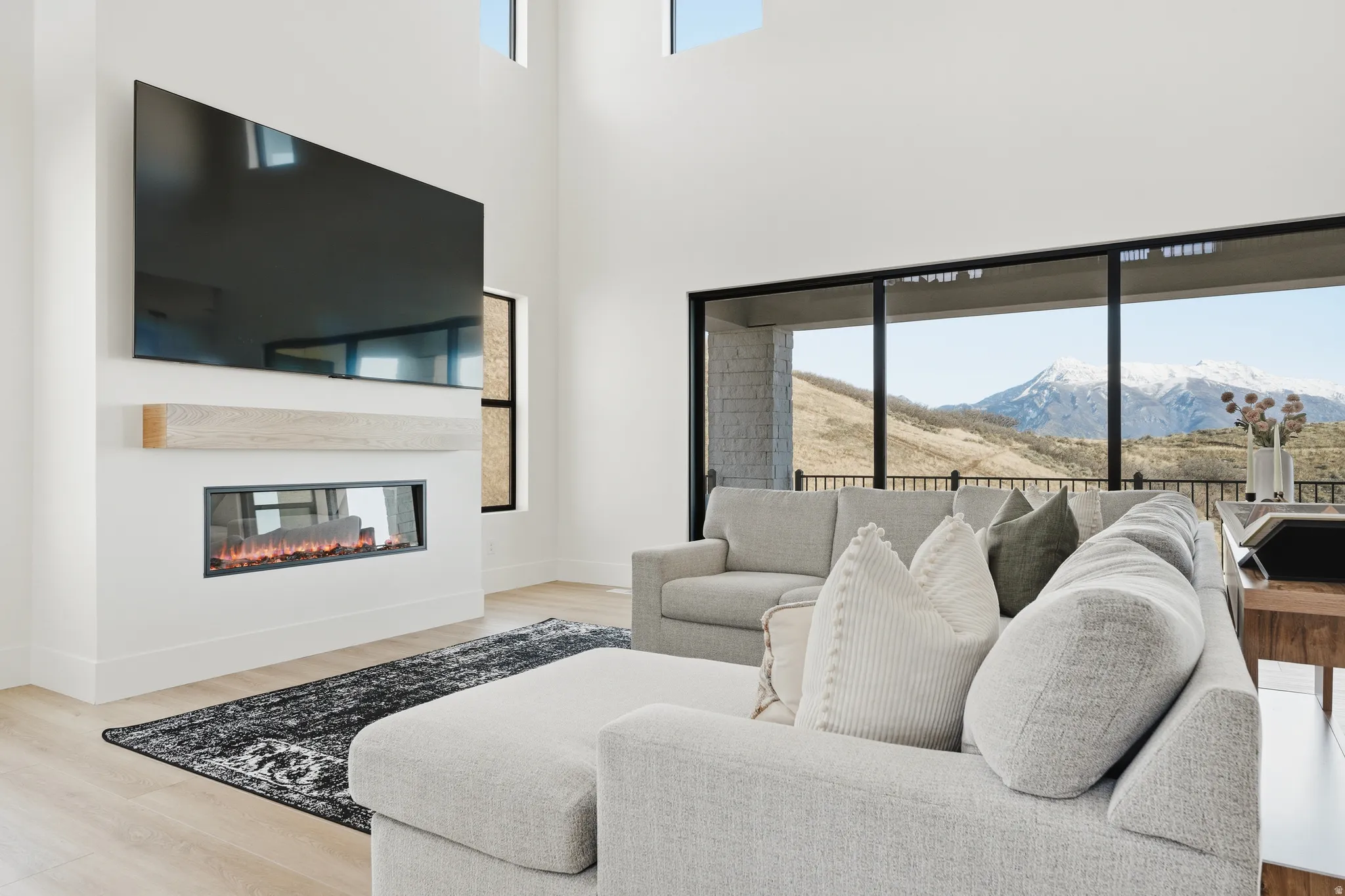 Living room featuring a mountain view, light wood-style floors, a glass covered fireplace, and a high ceiling