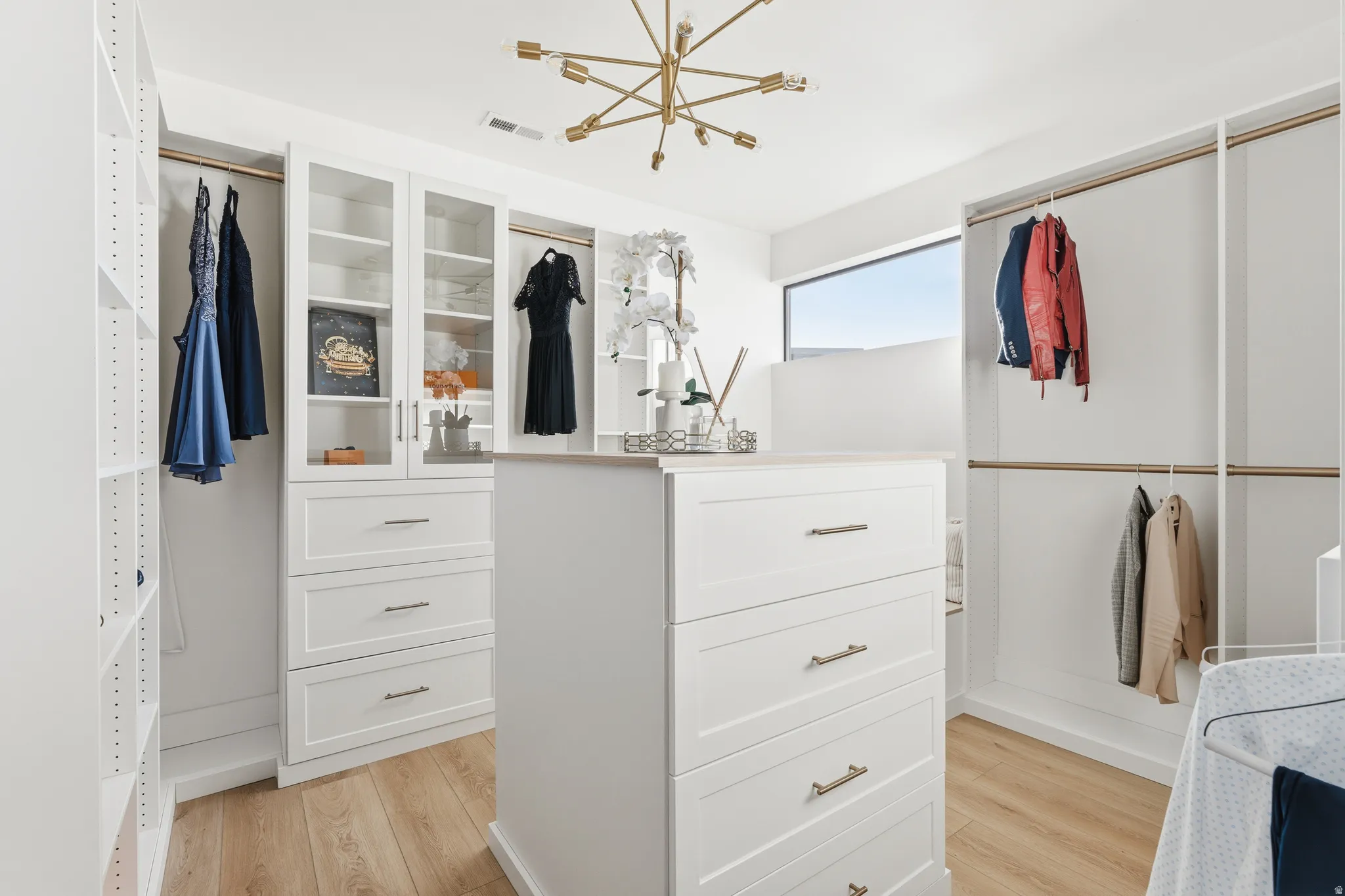 Walk in closet with light wood finished floors and suspended lighting