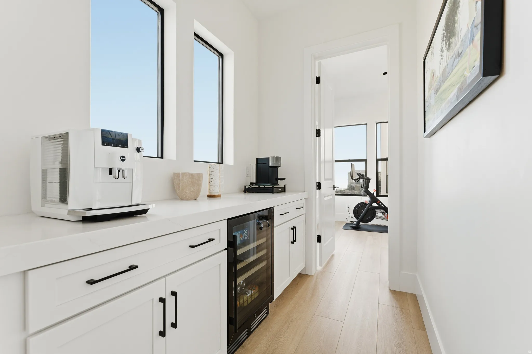 Bar area with white cabinets, wine cooler, light wood-style floors, and light stone counters