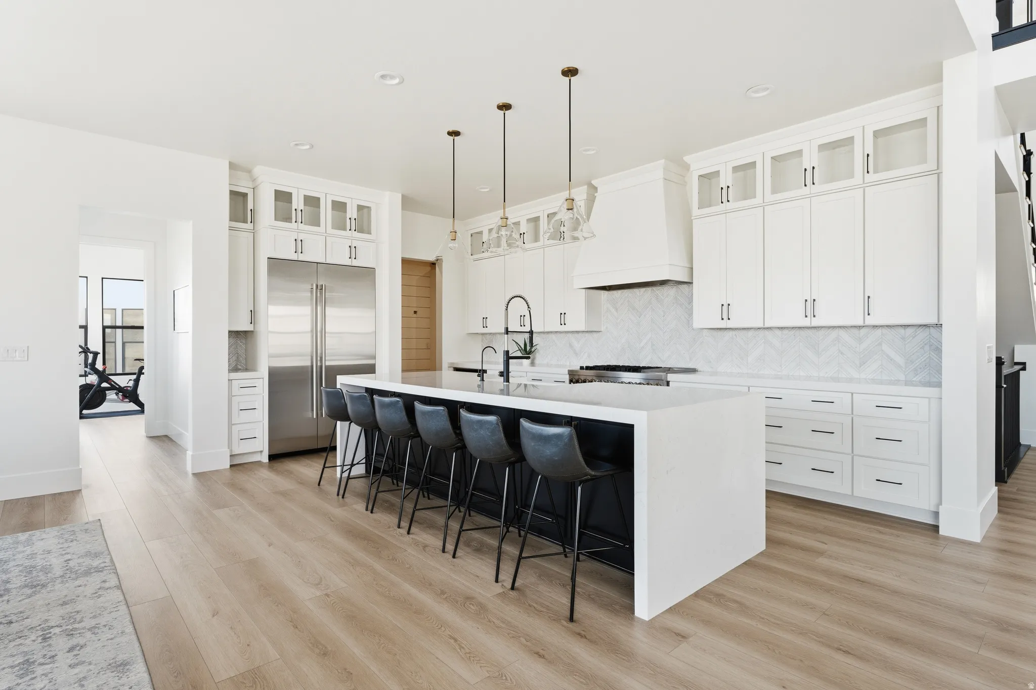 Kitchen featuring glass fronted cabinets, stainless steel built in refrigerator, hanging light fixtures, and light stone countertops