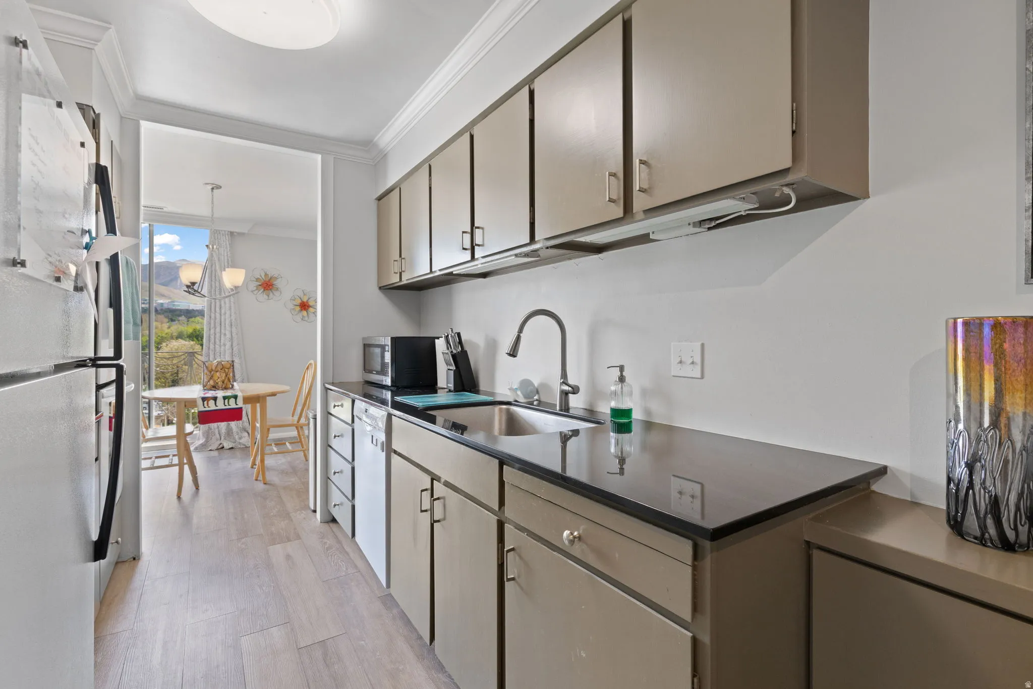 Kitchen featuring ornamental molding, white appliances, light wood-style flooring, pendant lighting, and expansive windows