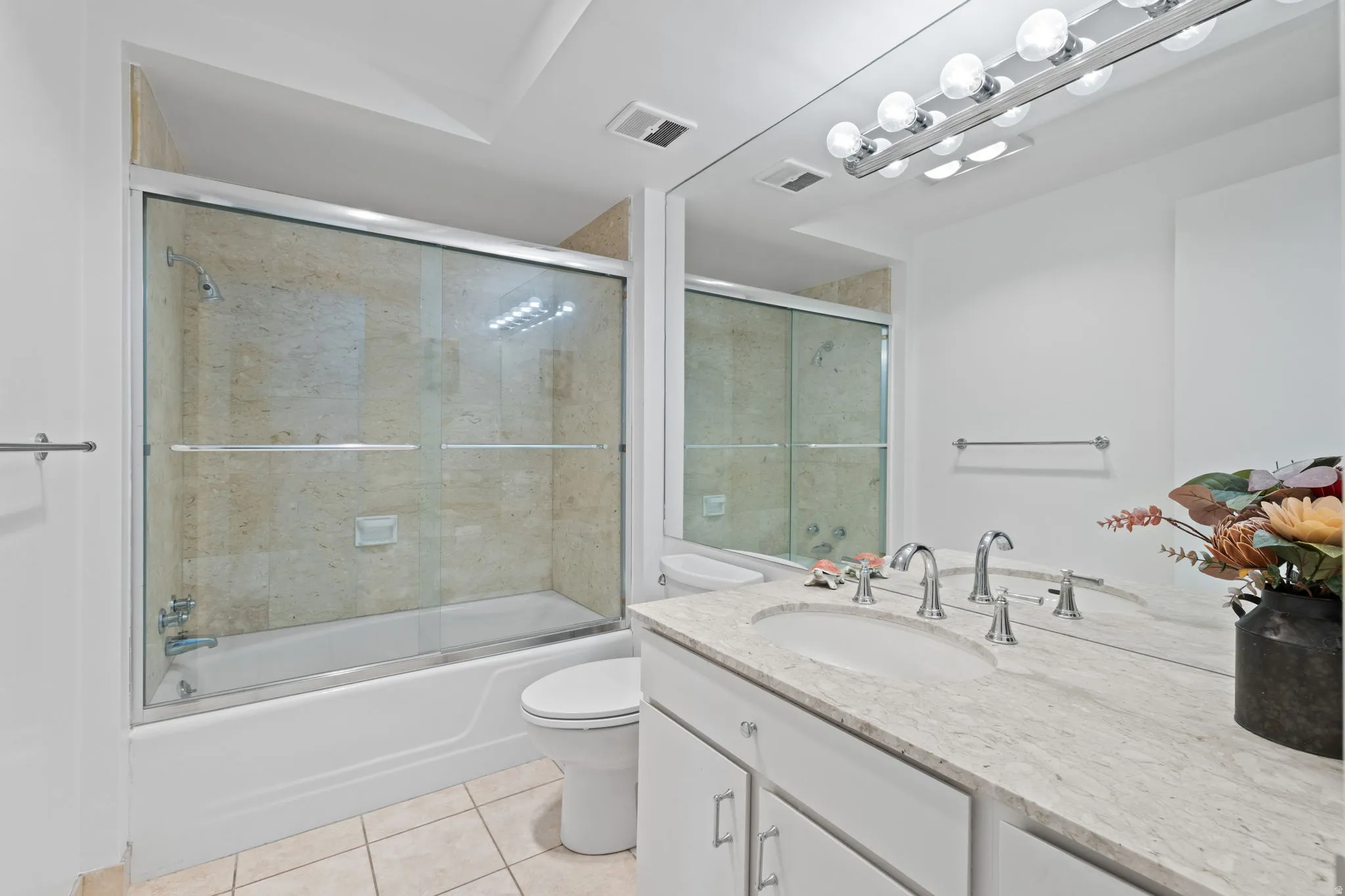 Bathroom featuring vanity, light tile patterned flooring, and bath / shower combo with glass door