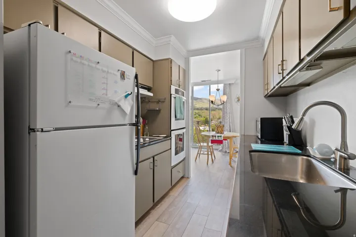 Kitchen with white appliances, ornamental molding, hanging light fixtures, dark countertops, and floor to ceiling windows