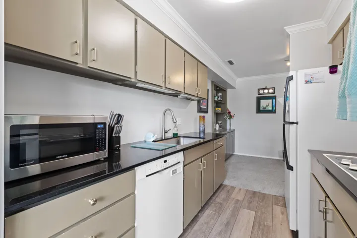 Kitchen featuring crown molding, white appliances, light wood-style floors, and dark stone counters
