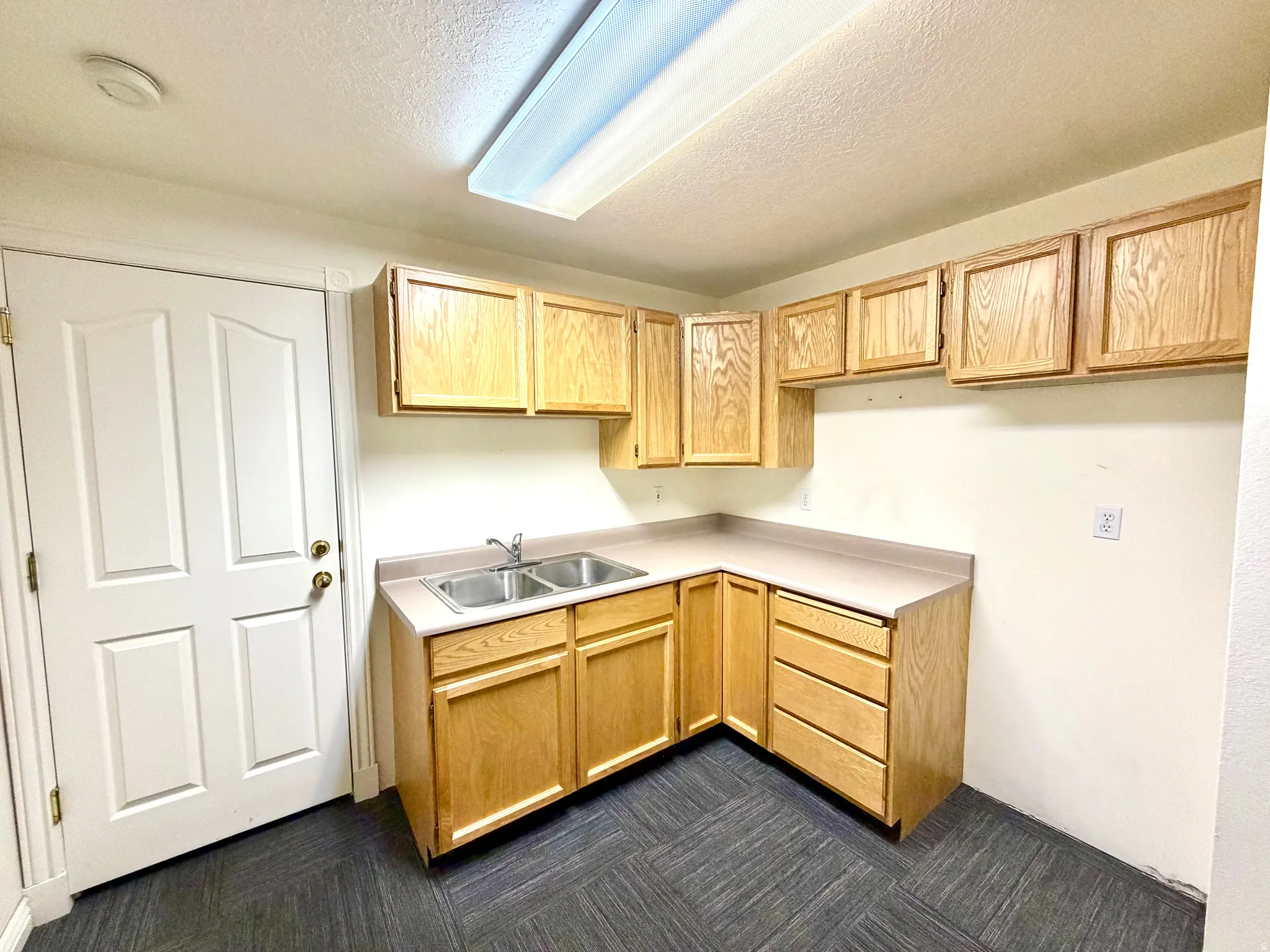 Kitchen featuring light wood finish cabinetry, a textured ceiling, light countertops, and dark carpet