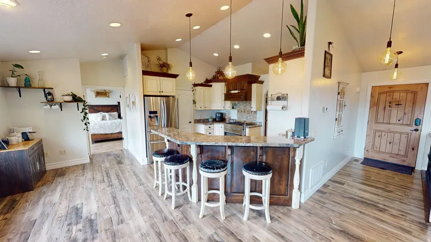 Kitchen featuring a kitchen breakfast bar, vaulted ceiling, light stone counters, stainless steel appliances, and light wood-type flooring