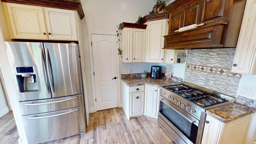 Kitchen with stainless steel appliances, light wood-style floors, tasteful backsplash, and dark stone countertops