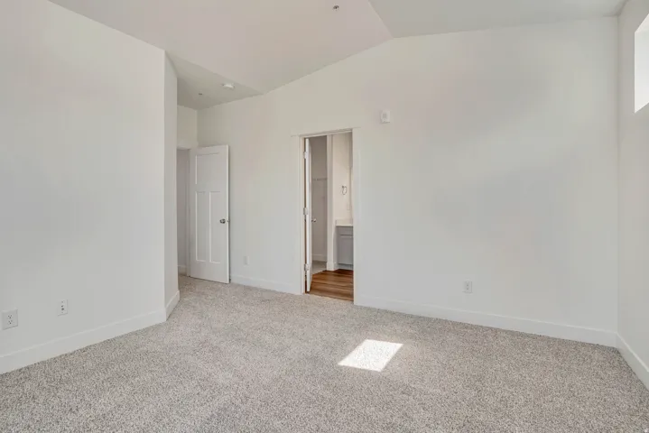 Unfurnished bedroom with vaulted ceiling, light colored carpet, and ensuite bath