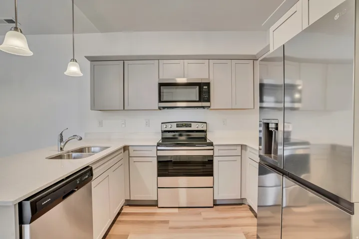 Kitchen featuring stainless steel appliances, a peninsula, light stone counters, pendant lighting, and light wood-style floors