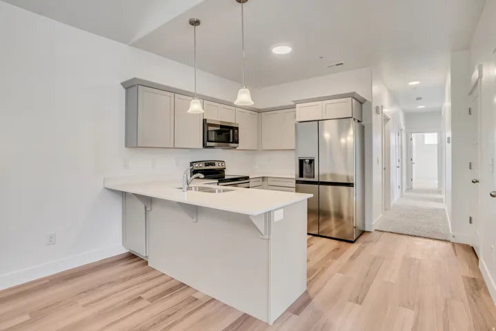 Kitchen with a peninsula, stainless steel appliances, a kitchen breakfast bar, decorative light fixtures, and light stone countertops