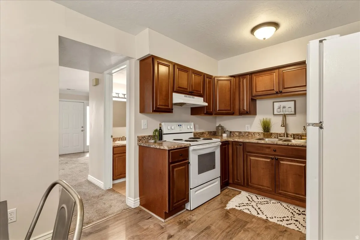 Kitchen with white appliances, light wood finished floors, light colored carpet, a textured ceiling, and wood finish cabinetry