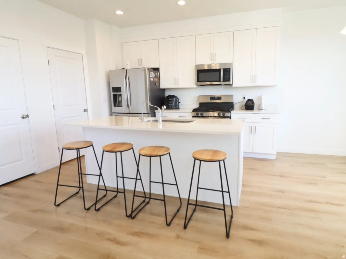 Kitchen with stainless steel appliances, light wood-type flooring, a kitchen island with sink, white cabinets, and a kitchen bar