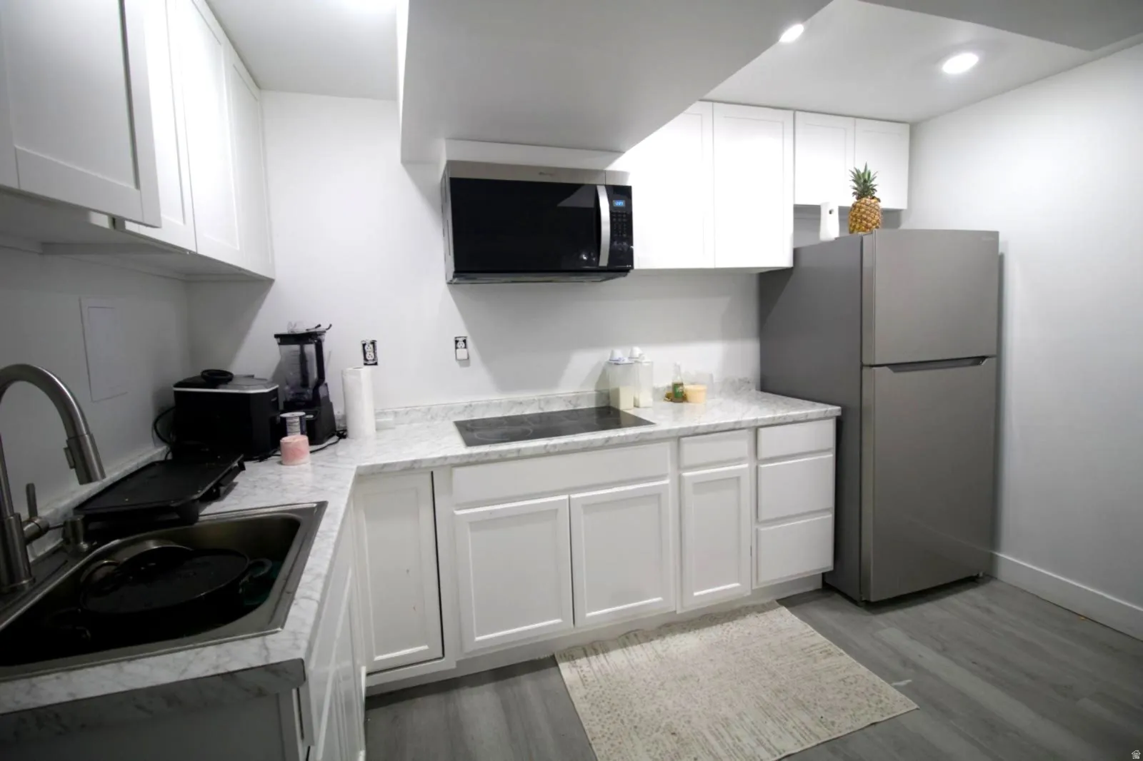 Contemporary kitchen featuring white shaker cabinetry, light-toned countertops, stainless steel appliances, and wood-finish flooring