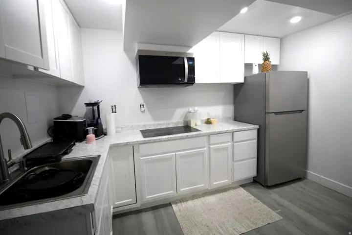 Contemporary kitchen featuring white shaker cabinetry, light-toned countertops, stainless steel appliances, and wood-finish flooring