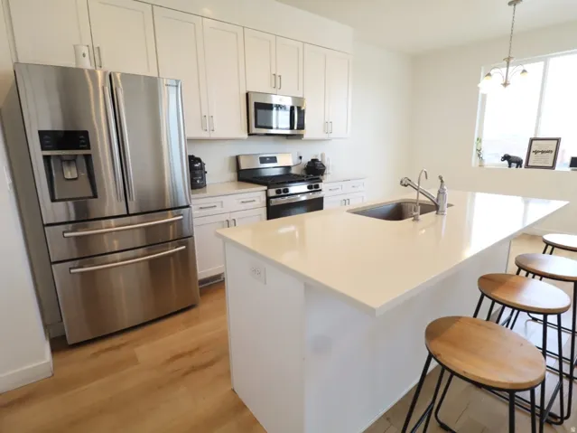 Kitchen with stainless steel appliances, a kitchen breakfast bar, an island with sink, light wood finished floors, and white cabinets