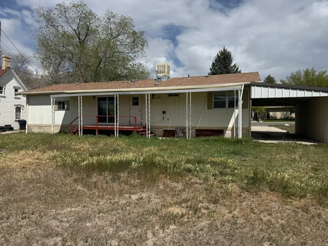 Rear view of property featuring an attached carport, a shingled roof, a porch, and a yard