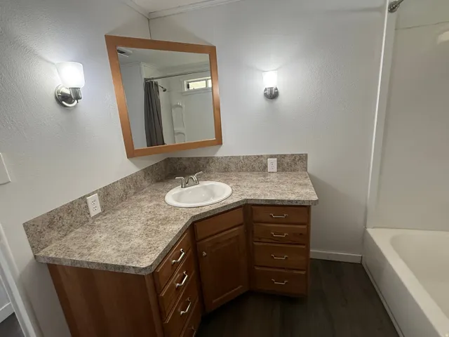 Full bathroom with vanity, a textured wall, dark wood finished floors, and shower / bath combination with curtain