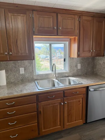 Kitchen with light countertops, stainless steel dishwasher, wood finish cabinetry, dark wood-style flooring, and tasteful backsplash