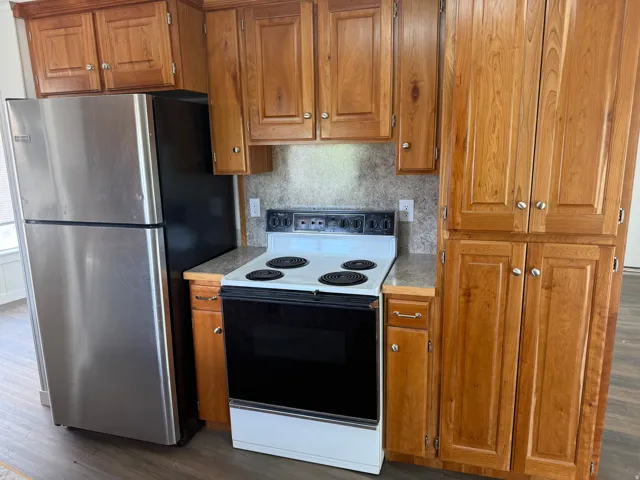 Kitchen featuring range with electric cooktop, wood finish cabinets, freestanding refrigerator, dark wood-style flooring, and light countertops