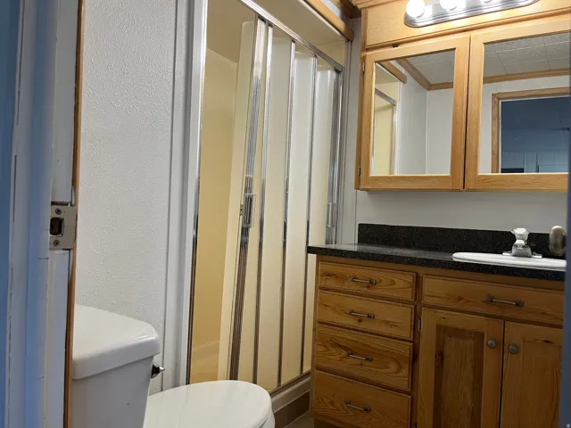 Bathroom featuring a wood-finish vanity with a dark countertop, an integrated sink, and an accordion-style shower enclosure