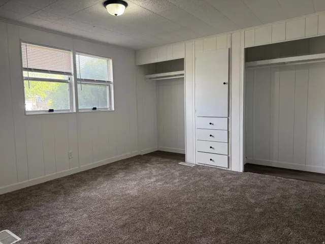 Unfurnished bedroom with two closets, dark colored carpet, and wood walls