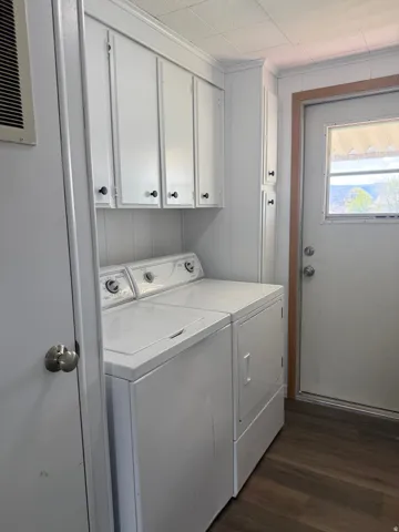 Laundry area featuring dark wood finished floors, separate washer and dryer, cabinet space, and wooden walls
