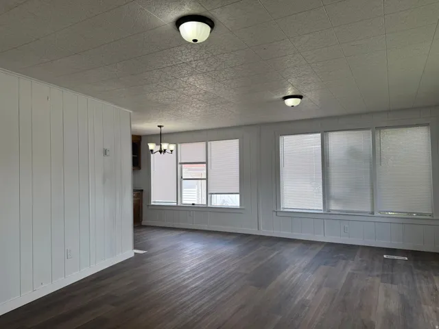 Empty room with dark wood-style flooring and a chandelier