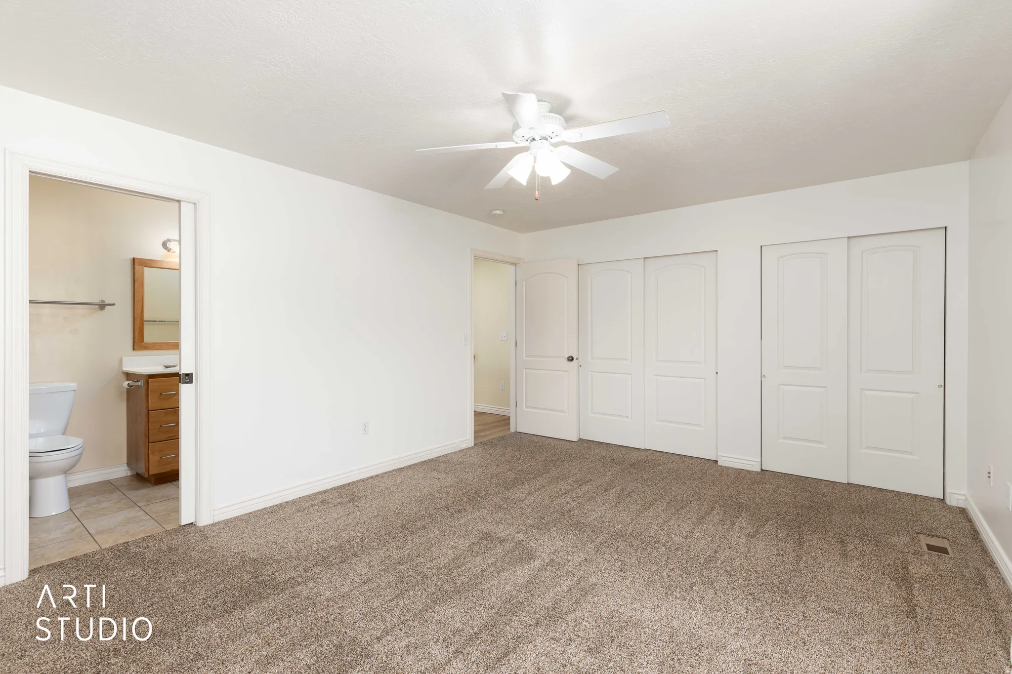 Unfurnished bedroom with two closets, light carpet, connected bathroom, and a ceiling fan