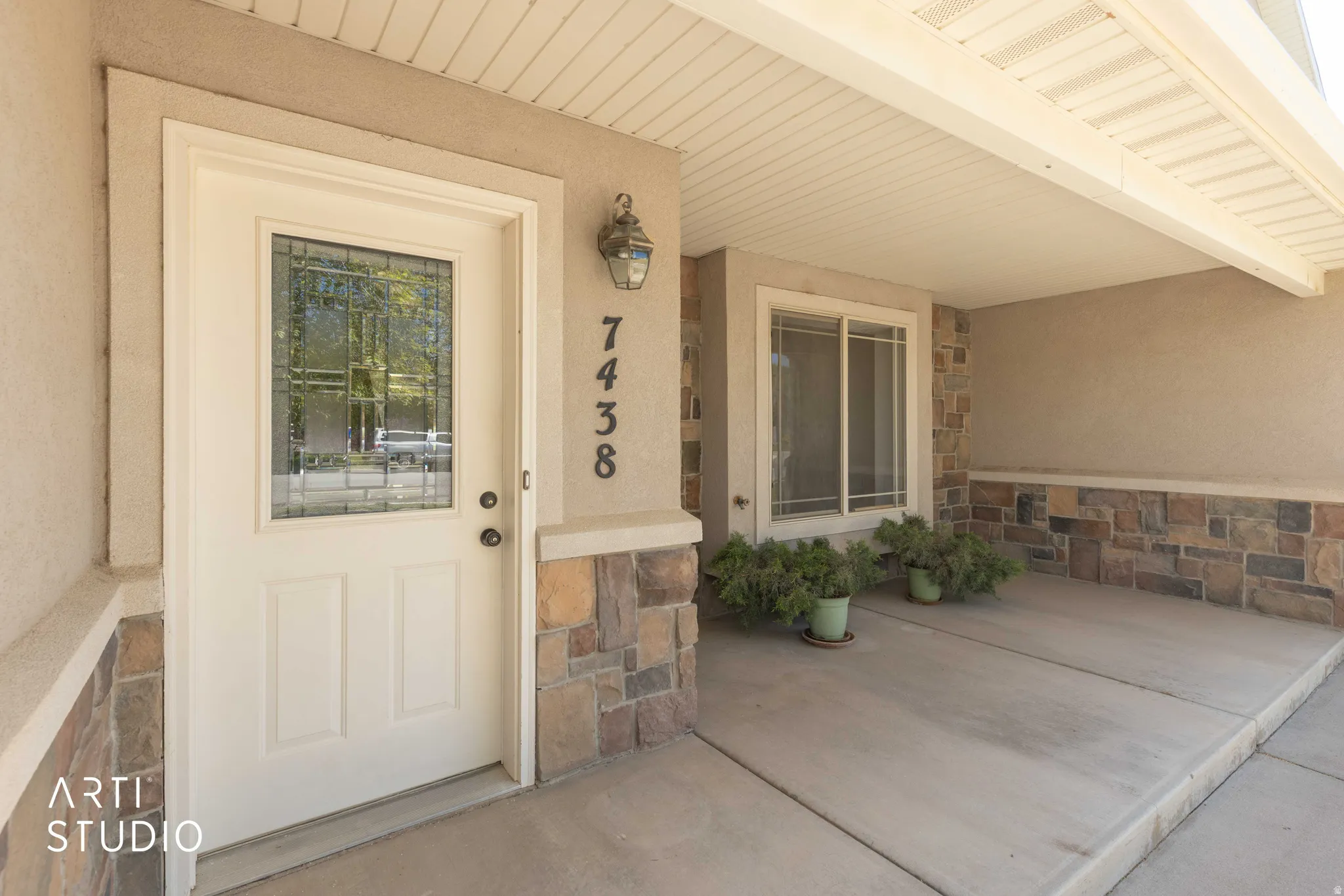 Doorway to property featuring stone siding, covered porch, and stucco siding
