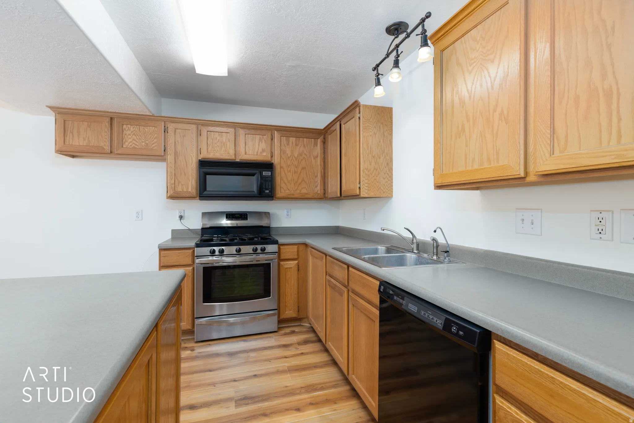 Kitchen featuring black appliances, light wood-style flooring, light countertops, a textured ceiling, and rail lighting