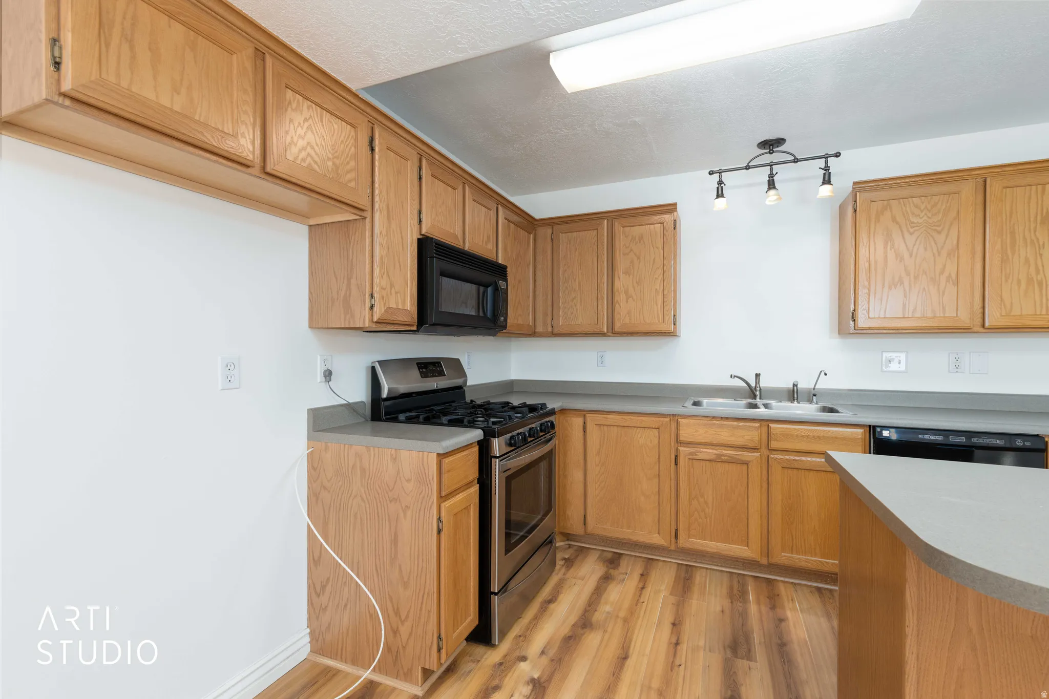 Kitchen with black appliances, light wood finished floors, light countertops, and a textured ceiling