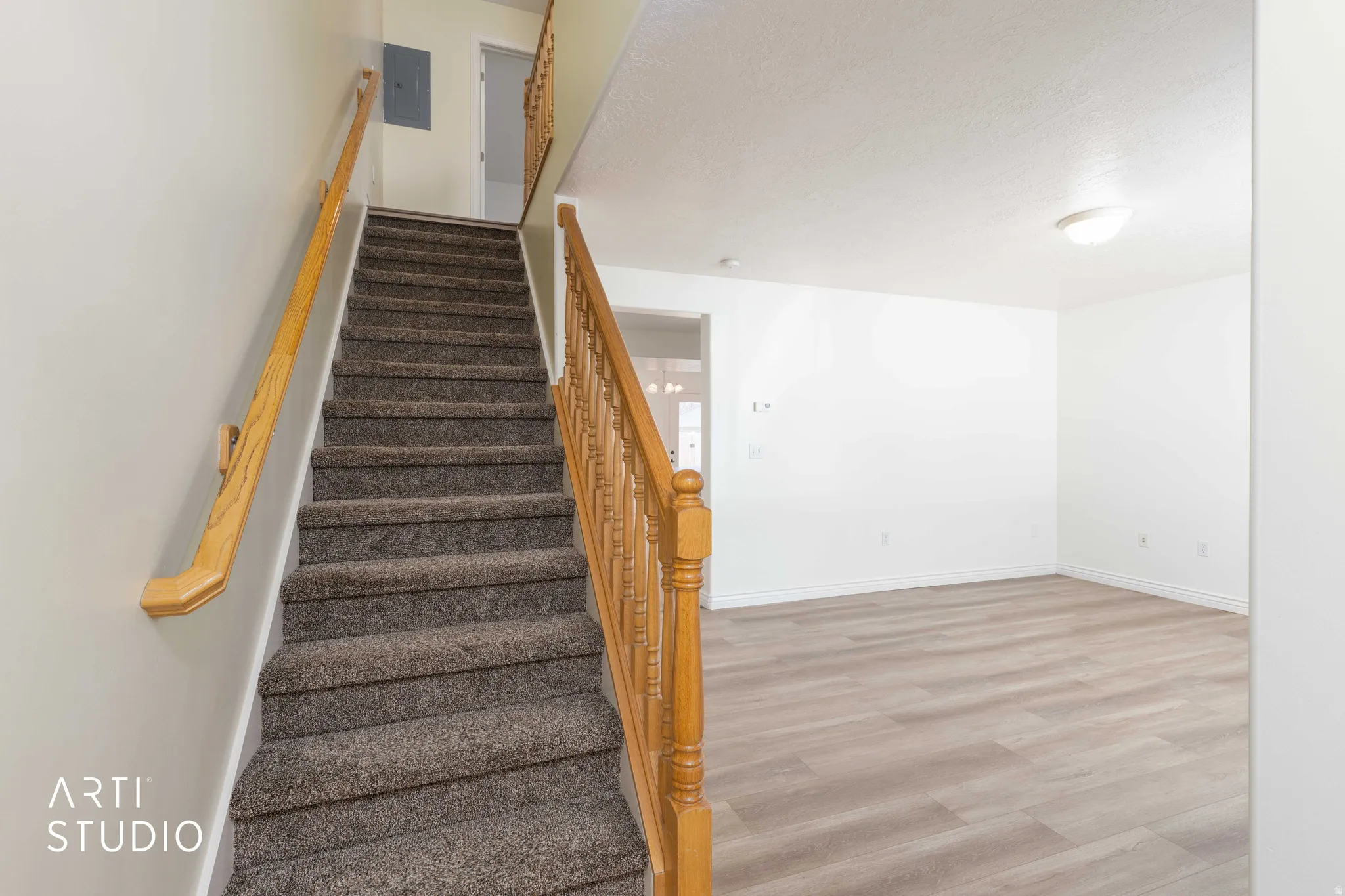 Staircase with wood finished floors, a textured ceiling, and electric panel