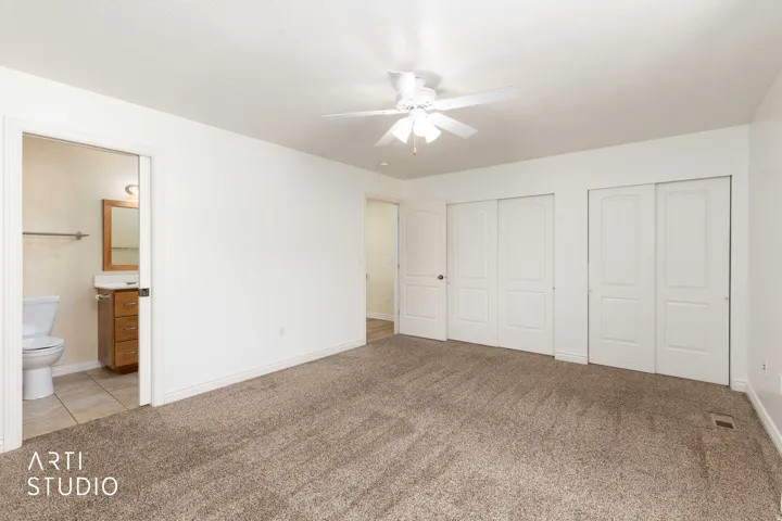 Bedroom with two closets, light carpet, connected bathroom, and a ceiling fan