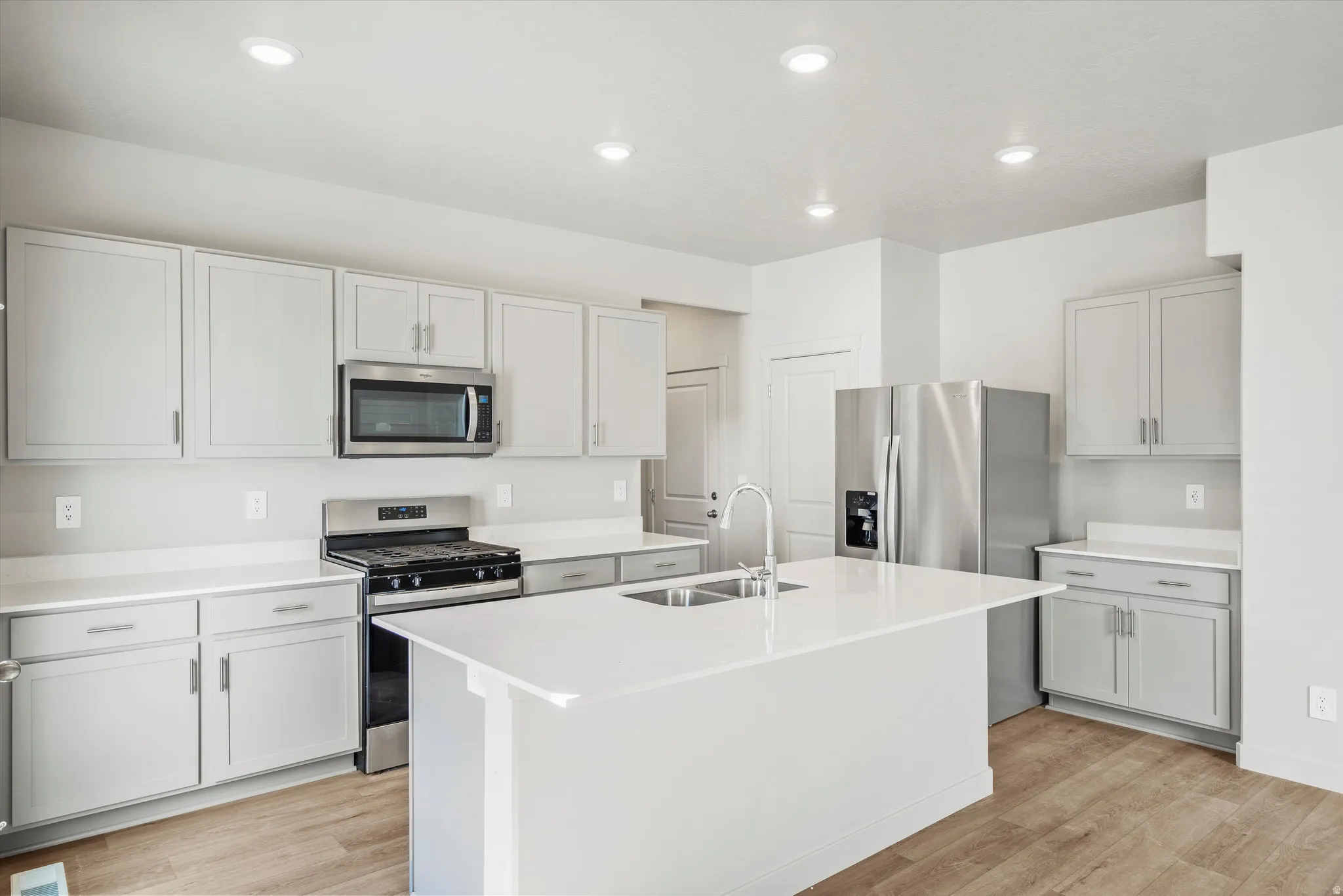 **DISCLAIMER** Interior package & color may vary. Kitchen with stainless steel appliances, a kitchen island with sink, light wood-type flooring, light stone countertops, and recessed lighting