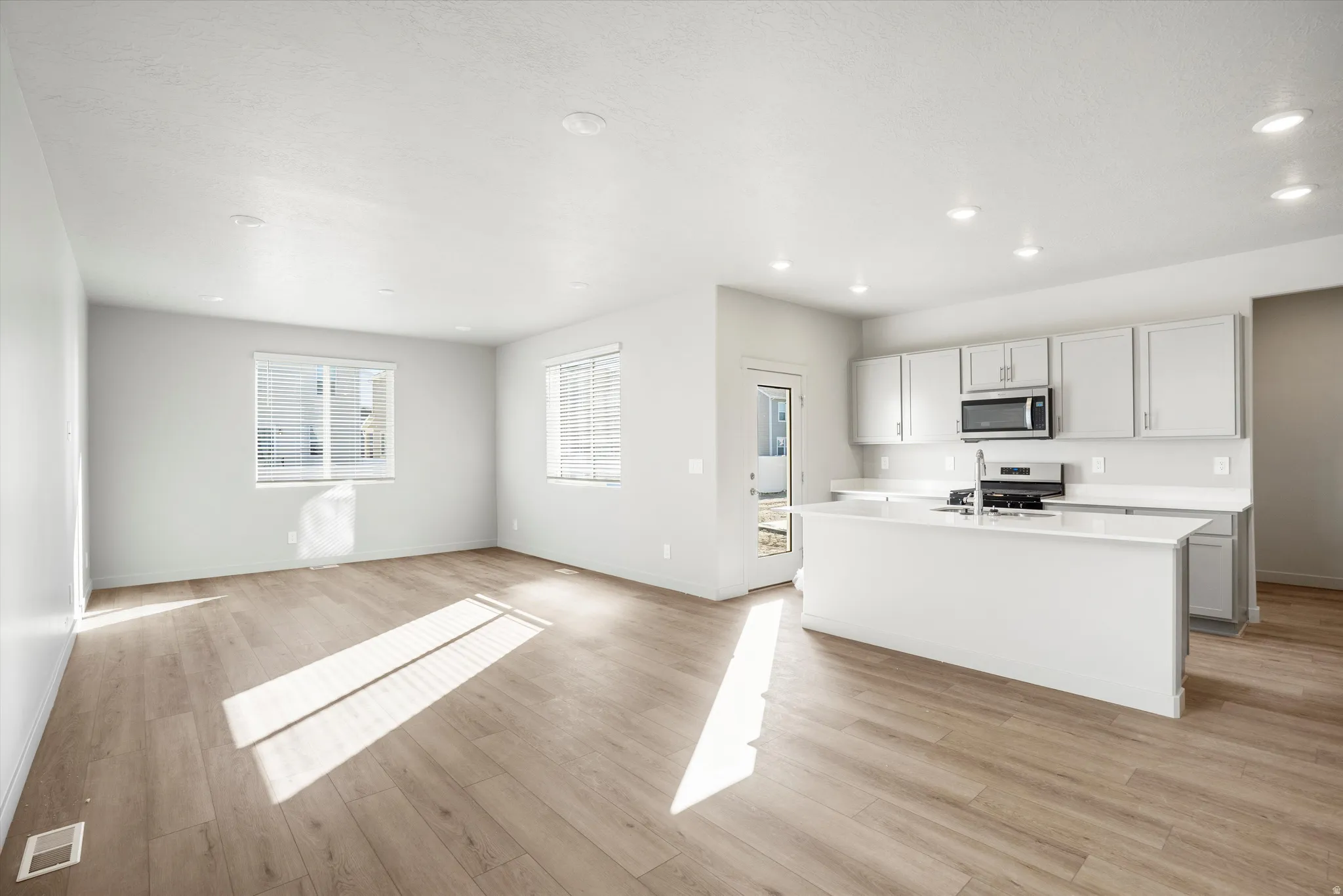 **DISCLAIMER** Interior package & color may vary. Kitchen with a kitchen island with sink, light wood-style flooring, open floor plan, gas stove, and stainless steel microwave