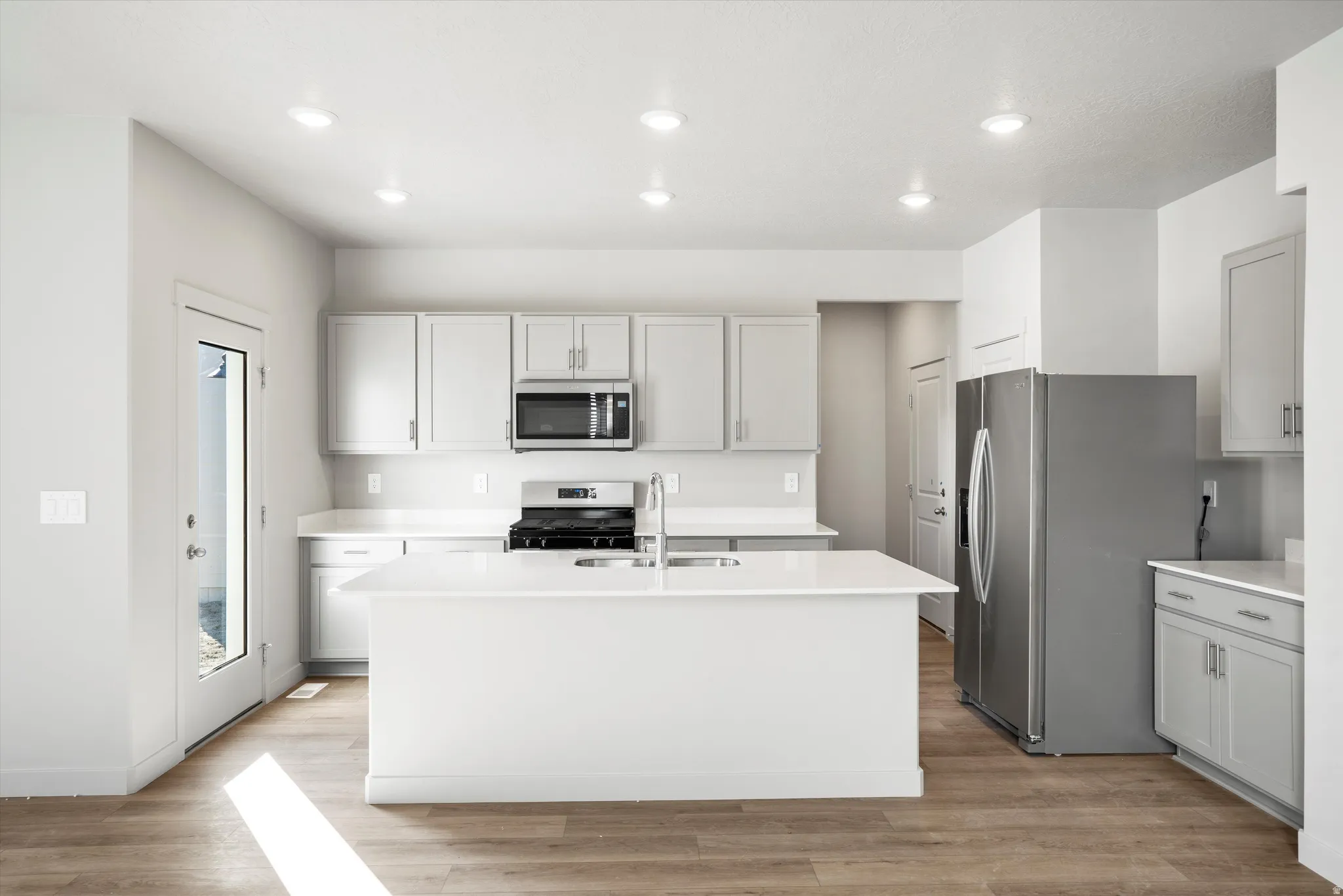 **DISCLAIMER** Interior package & color may vary. Kitchen featuring stainless steel appliances, a center island with sink, light wood-type flooring, light stone counters, and recessed lighting