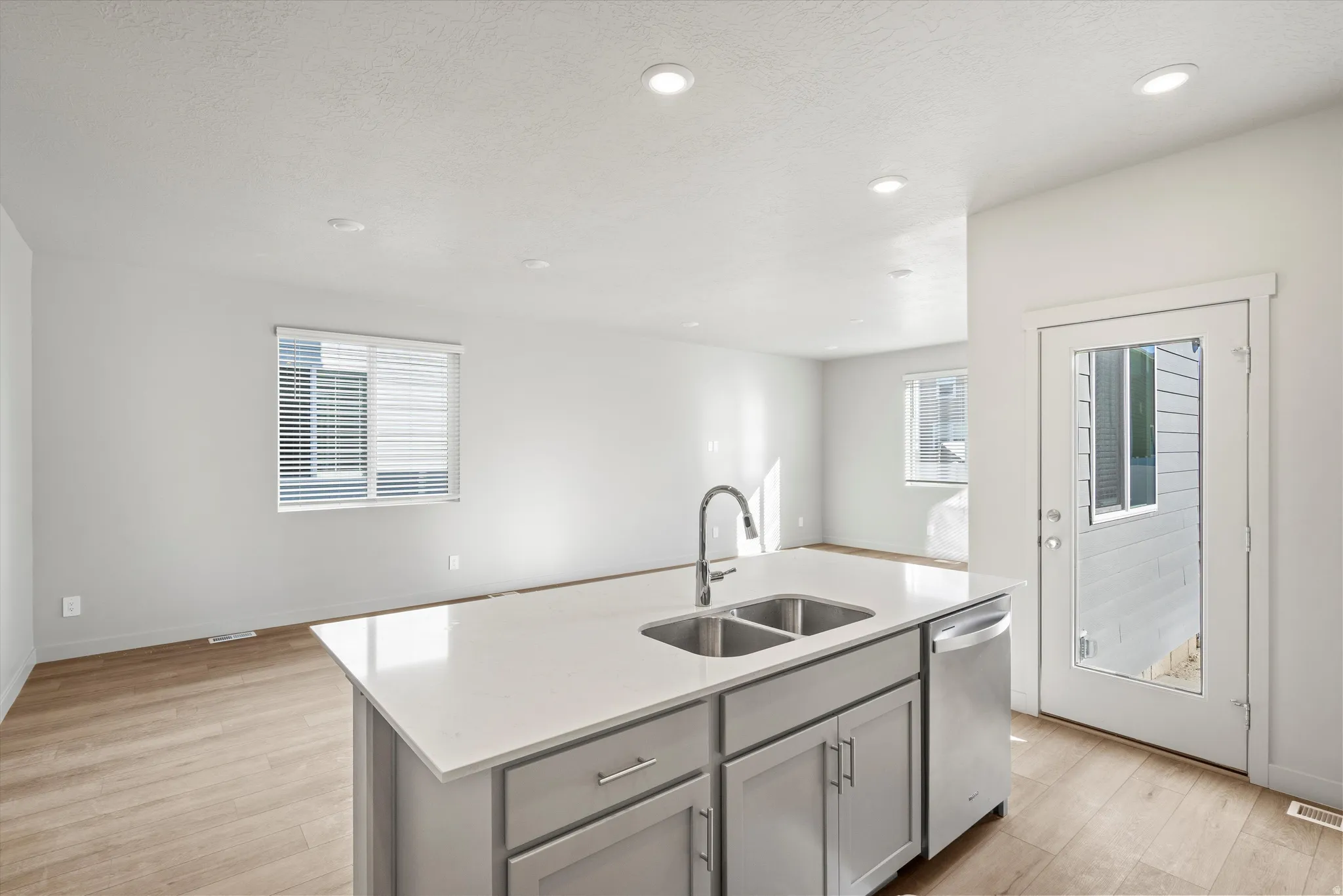 **DISCLAIMER** Interior package & color may vary. Kitchen featuring an island with sink, light wood finished floors, gray cabinets, light stone counters, and open floor plan